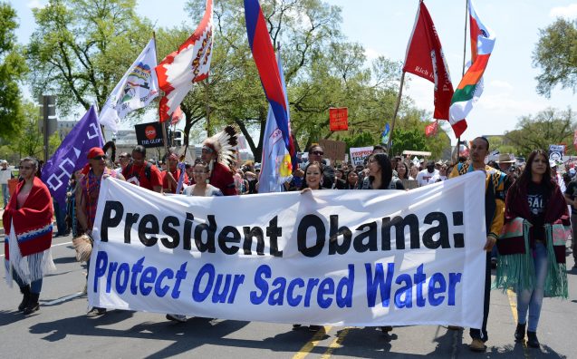 protestors hold sign that says 'president obama: protect our sacred water'