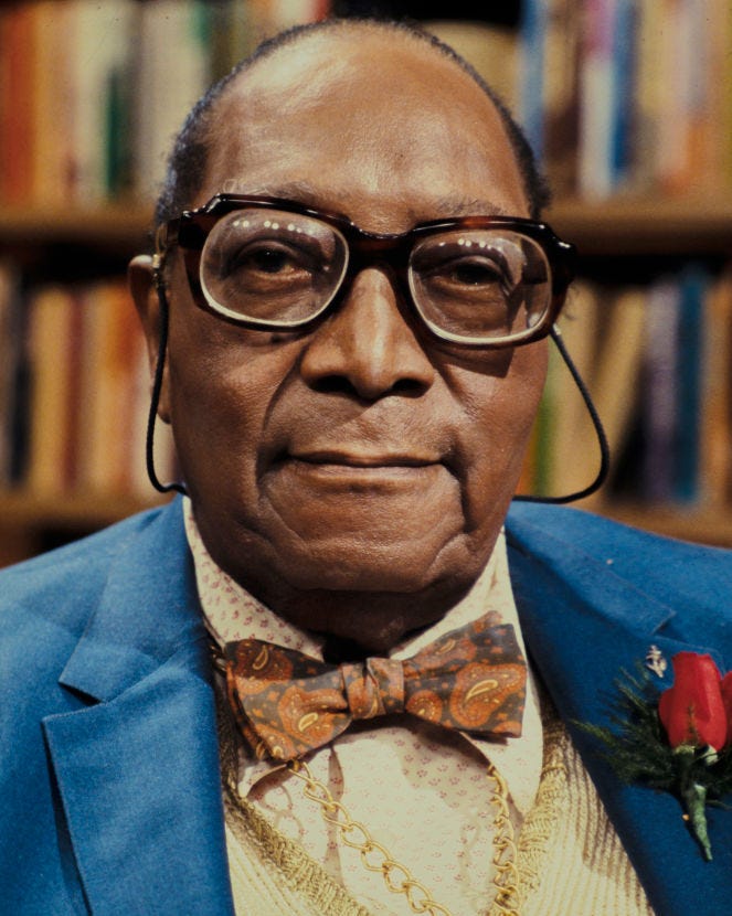 james van der zee wearing stringed glasses and taking a photo in front of bookshelves in the background