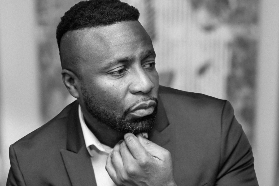 A black and white photo of a Black man wearing a suit with a hand on his chin.