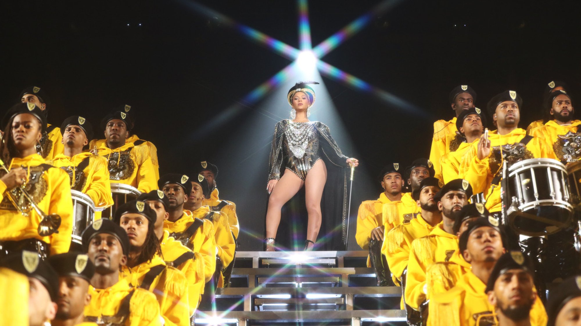 Beyonce stands onstage, surrounded by performers in yellow, in 