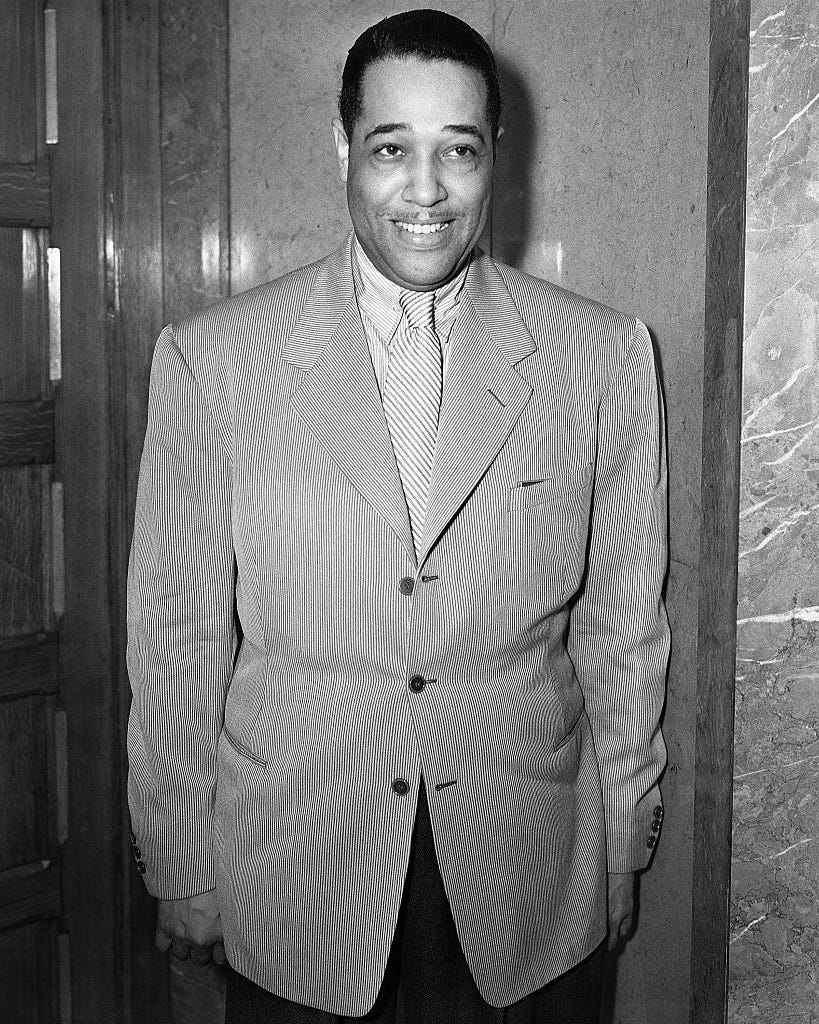 duke ellington smiling as he stands with his arms at his sides in a photo