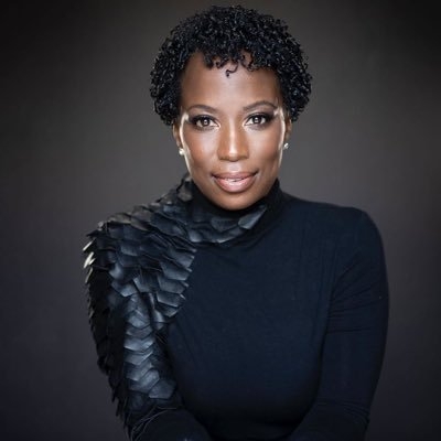 Black lady with short curls, dark swaether and dark background.